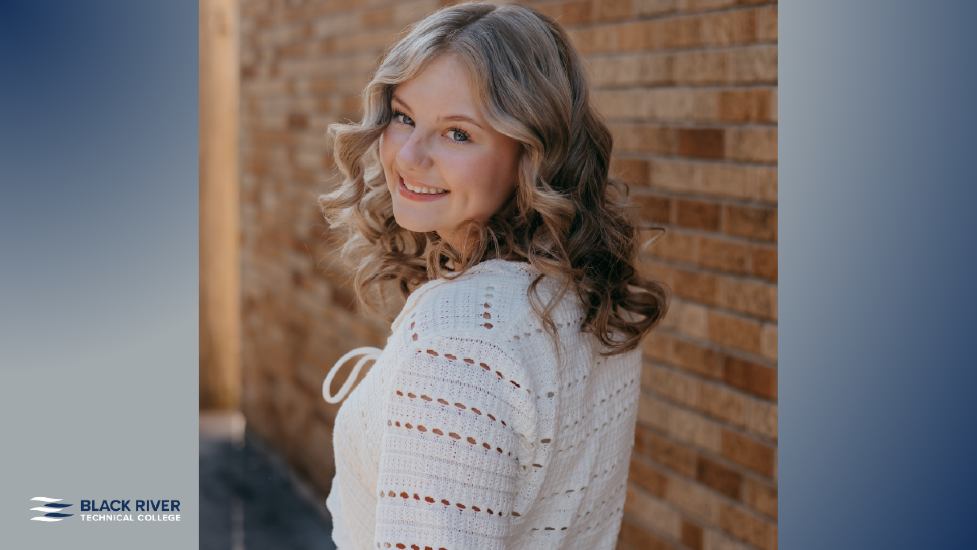 A young woman with curly blonde hair, wearing a white knit top, smiles over her shoulder against a brick wall backdrop, with Black River Technical College branding.